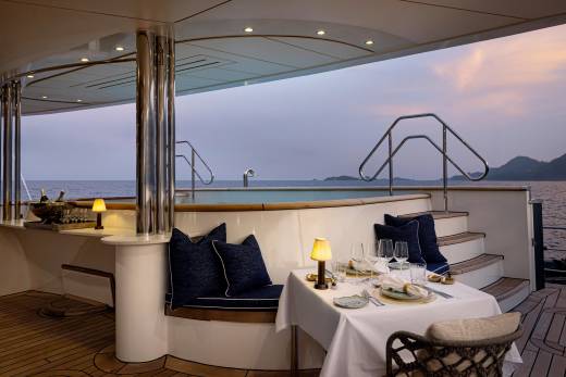 A luxurious yacht interior with a dining area, comfortable seating, and a scenic view of the ocean and mountains in the background.