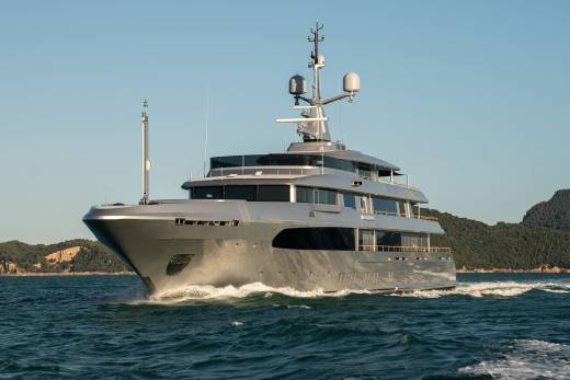 A large, luxurious yacht navigates the open waters, surrounded by a picturesque coastal landscape in the background.