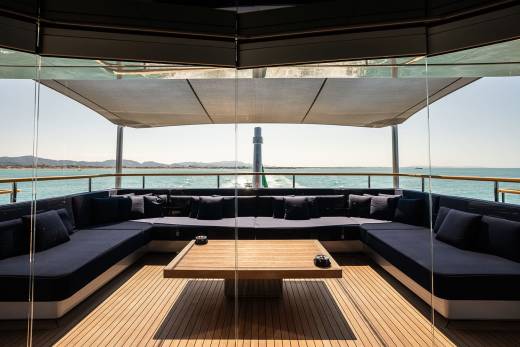 A modern, glass-enclosed lounge area with comfortable seating and a wooden table, overlooking a scenic coastal landscape.