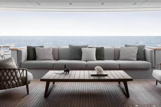 A cozy outdoor seating area with a large gray sofa, wooden coffee table, and wicker chairs overlooking the serene ocean in the background.
