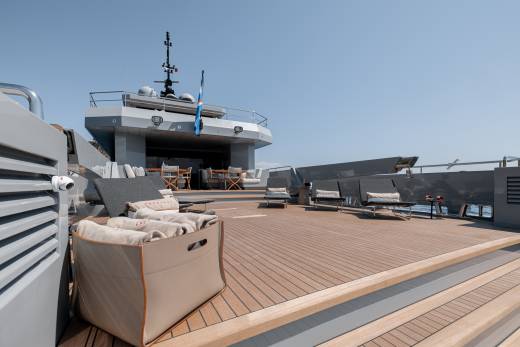 A large yacht with a spacious deck featuring comfortable seating areas and a raised command bridge, set against a clear blue sky.