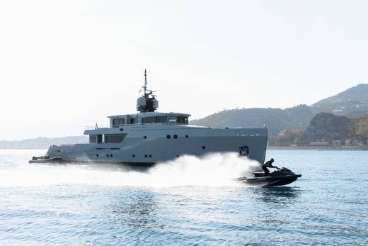 A large gray yacht is sailing on a calm body of water, with a smaller boat in the foreground and mountains in the background.