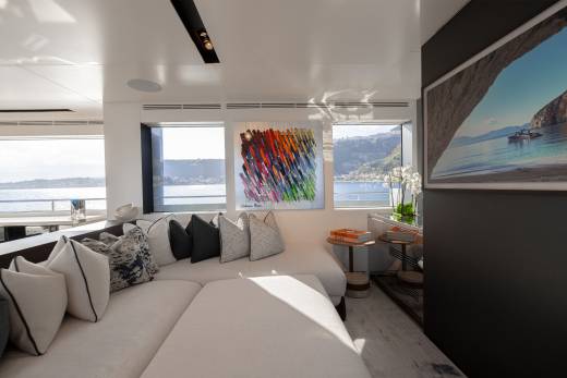 A cozy living room with a large, comfortable sofa, colorful abstract artwork on the wall, and a scenic view of a body of water and mountains in the background.