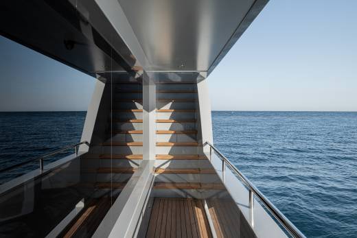 A wooden staircase leads down to the vast, serene expanse of the open ocean, with the horizon visible in the distance.