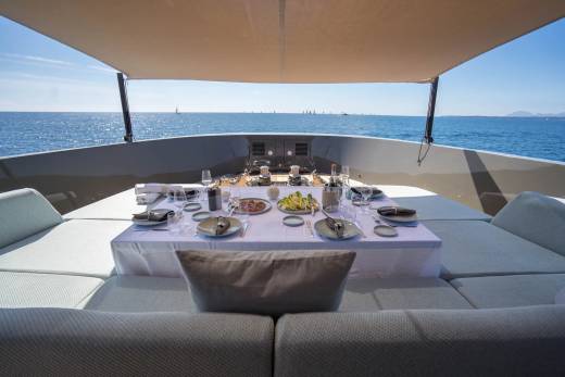 A beautifully set dining table on a yacht's deck overlooks a calm blue sea dotted with sailboats.