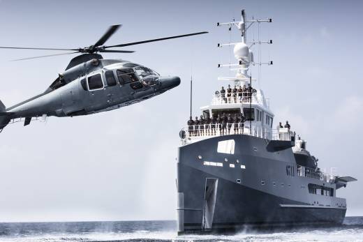 A helicopter flies over a large yacht sailing on the ocean.