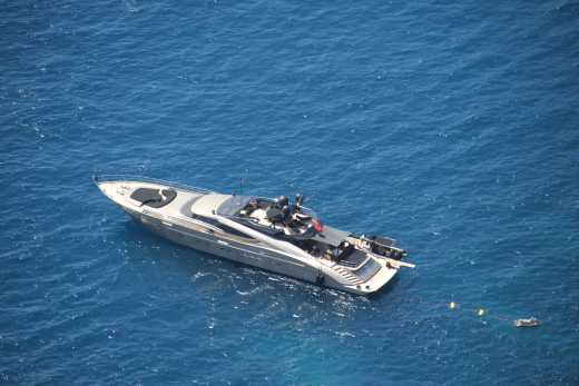 A sleek white yacht floats on the deep blue ocean, with a small dinghy tethered nearby.