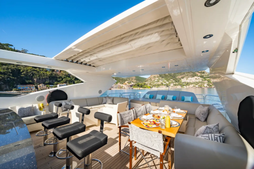 A luxurious yacht deck with a bar and dining area in the foreground overlooks a scenic coastal town in the background.