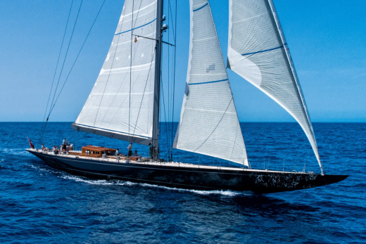 A majestic dark sailboat with full sails glides across the deep blue ocean under a clear sky.