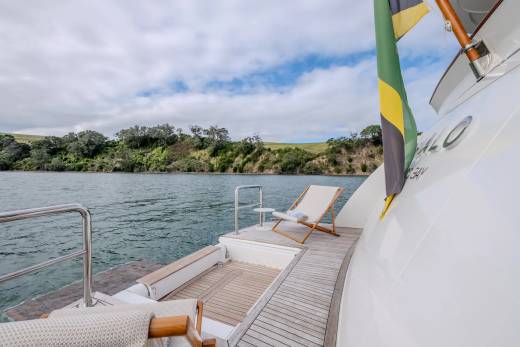 Two lounge chairs sit on the deck of a yacht with a lush, green coastline in the background.