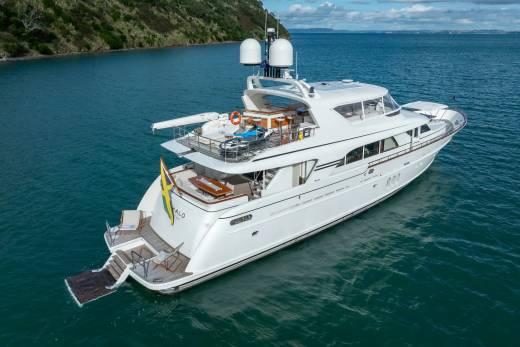A luxurious white yacht with a Jamaican flag is anchored in calm blue water, with a lush green hillside in the background.