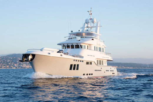 A large white yacht cruises on calm blue water with a hazy coastline in the background under a clear sky.