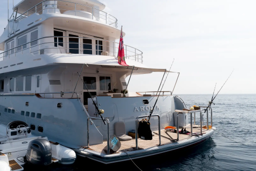 A large white yacht with fishing rods on its deck floats on calm blue water under a bright sky.