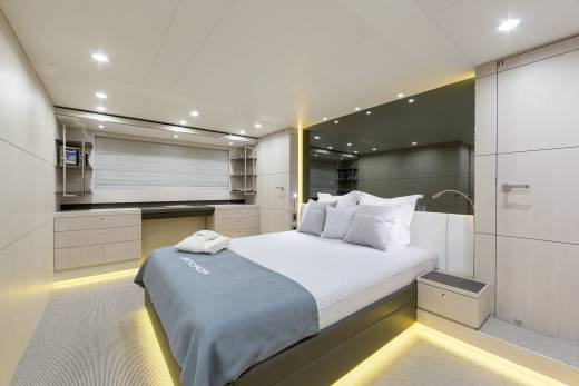 A luxurious bedroom with a neatly made bed in the foreground and a mirrored wall reflecting shelves and cabinets in the background.