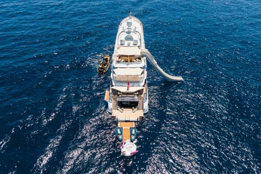 A large white yacht with a slide and a tender boat is anchored in the deep blue ocean.