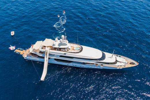 A large white yacht with a slide extending into the deep blue ocean is surrounded by people enjoying water activities.