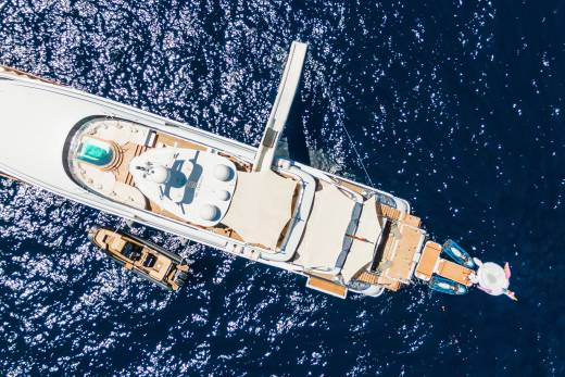 A large white yacht with a slide and a smaller boat beside it floats on the deep blue ocean.