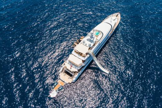 A large white yacht with a slide is anchored in the deep blue ocean.