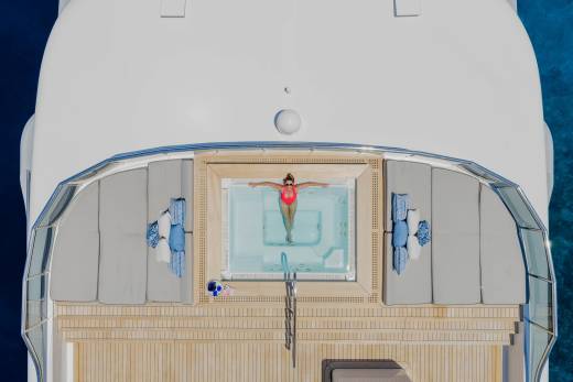 A woman in a red swimsuit relaxes in a jacuzzi on a yacht's deck, with the blue ocean visible in the background.