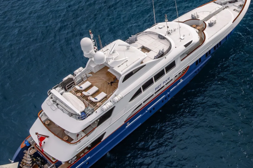 A luxurious white and blue yacht with lounge chairs on its deck sails on the deep blue ocean.