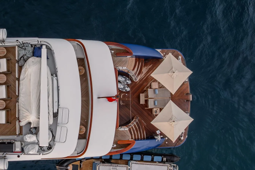 A luxurious yacht with white lounge chairs in the foreground is anchored in the deep blue sea.