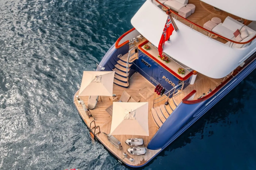 A luxurious yacht with white umbrellas and lounge chairs on its deck floats on calm blue water.