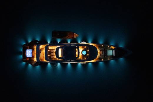 A luxurious yacht with illuminated decks and a smaller boat nearby floats on dark, calm water.