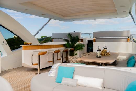 A luxurious yacht deck features a comfortable seating area in the foreground and a bar and dining table in the background, all under a covered canopy.