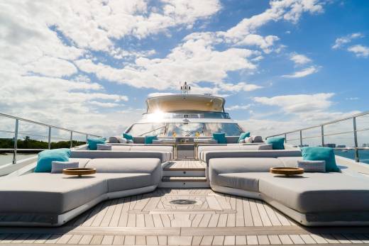 Plush lounge seating on a yacht's deck faces a bright sky with scattered clouds.