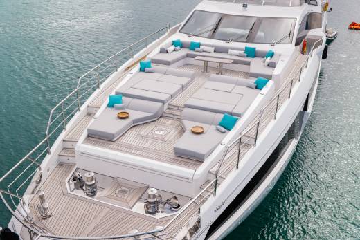 A luxurious white yacht with plush gray seating and bright turquoise cushions is docked in calm, blue water.