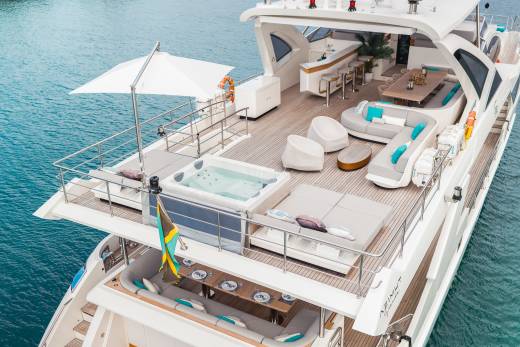 A luxurious yacht with a hot tub and lounge area in the foreground is anchored in calm blue water.