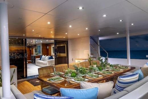 A beautifully set dining table on a yacht's deck is in the foreground, with the ocean and a twilight sky visible in the background.