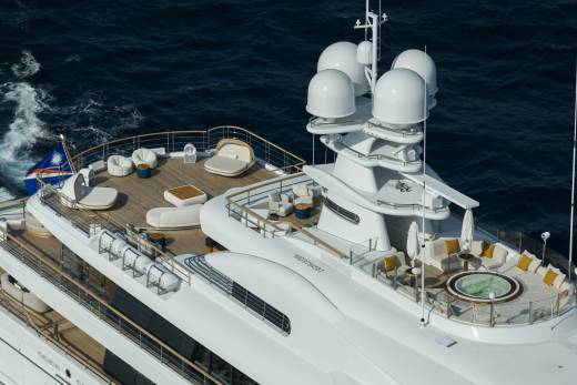 A luxurious white yacht with multiple decks of seating and a hot tub cruises through the deep blue ocean.