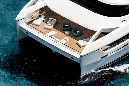 A luxurious white catamaran with plush seating on its deck cruises through turquoise waters.