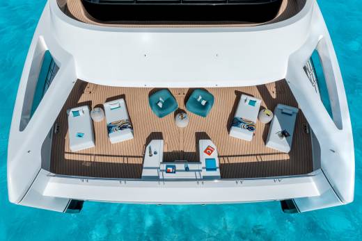 A luxurious white yacht with lounge chairs and sunbeds on its deck floats on crystal clear turquoise water.