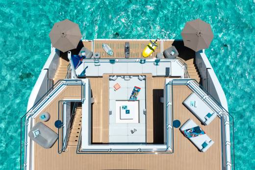 A luxurious yacht with lounge areas and water toys rests on crystal clear turquoise water.