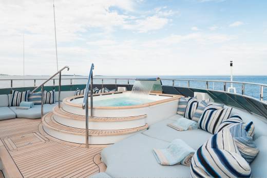 A luxurious yacht's sundeck features a bubbling jacuzzi with a waterfall in the foreground, while the background shows a calm blue ocean under a cloudy sky.