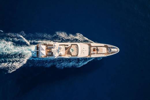 A luxurious white yacht cruises through deep blue water, leaving a frothy white wake behind it.