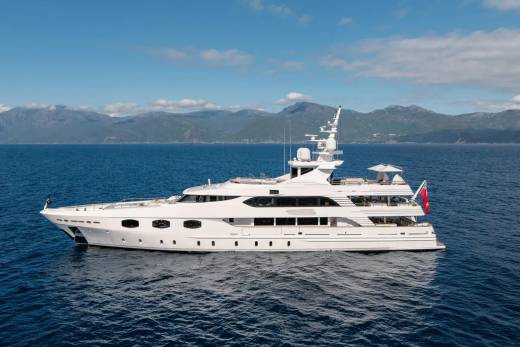A large white yacht floats on calm blue water in the foreground, with a backdrop of distant, hazy mountains under a clear blue sky.