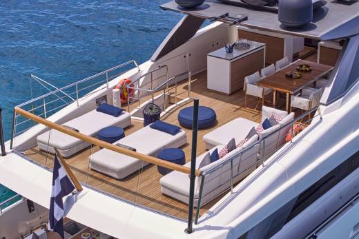 A luxurious yacht deck with lounge chairs and a dining area is anchored in clear blue water.