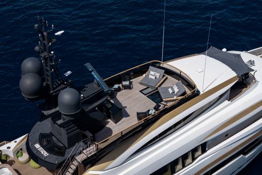 A luxurious yacht with a spacious deck furnished with lounge chairs and tables sits on the deep blue ocean.