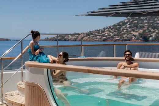 Three people relax in a hot tub on a yacht with a hillside town in the background.