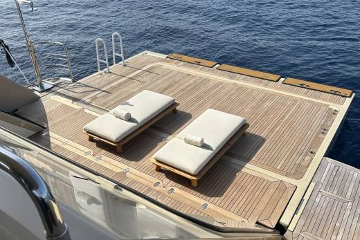Two empty lounge chairs sit on a wooden deck of a yacht, with the deep blue ocean stretching out in the background.