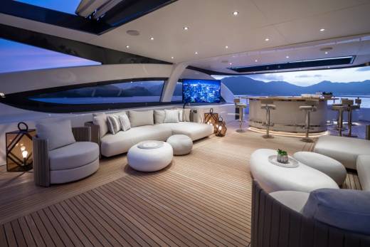 Luxurious outdoor seating and a bar area on a yacht deck are set against a twilight sky and distant mountains.