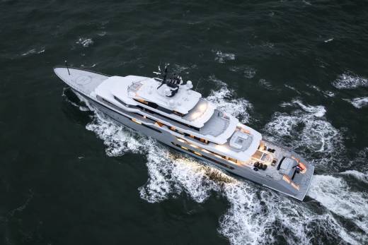A large, modern yacht cruises through choppy, dark water, leaving a white wake behind it.