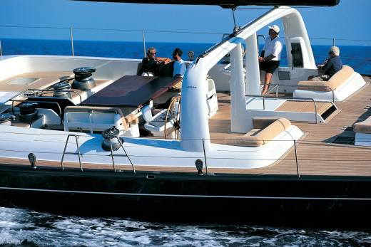 Four people relax on the deck of a large sailboat with the blue ocean stretching out behind them.