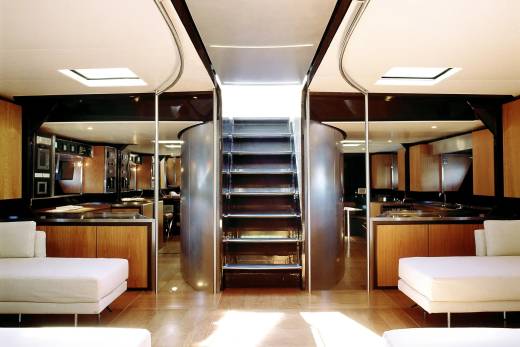 Two white sofas in the foreground face a central staircase with mirrored walls and wooden cabinetry in the background.