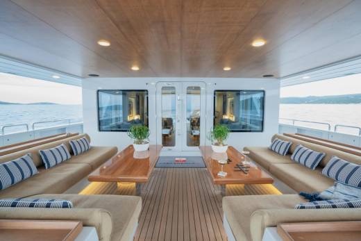 Luxurious outdoor seating with plush cushions and wooden tables fills the foreground, while the background reveals a serene ocean view with distant islands under a bright sky.