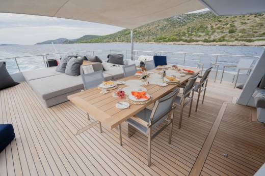 A set dining table on a yacht's deck is surrounded by a calm sea and a hilly coastline.