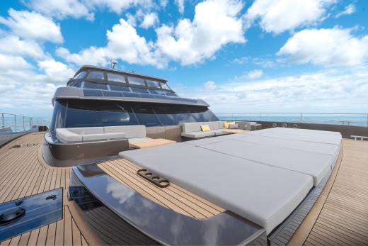 A luxurious yacht with a spacious deck and comfortable seating is anchored in the ocean under a cloudy blue sky.